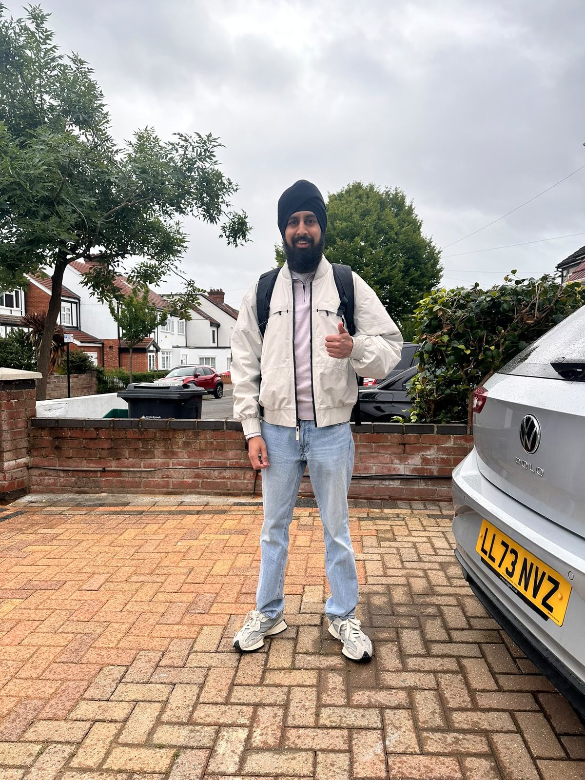 Nirmit standing on a driveway with a backpack, thumbs up